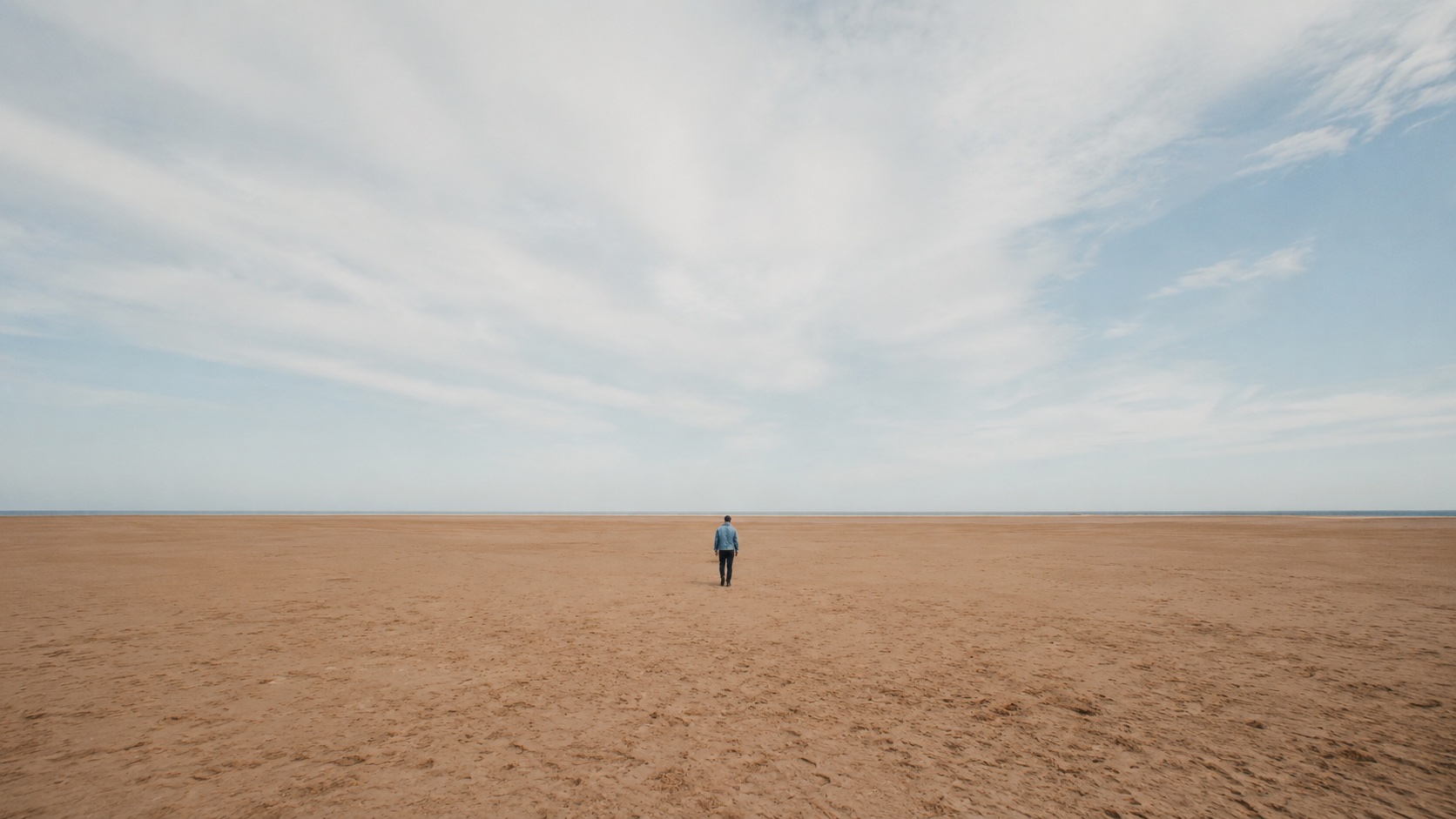 A person standing alone on a wide empty beach, looking toward the horizon